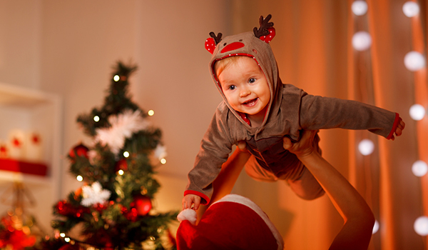 Adorable baby having fun near Christmas tree being lifted by someone and the baby enjoying