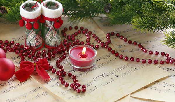 Christmas Carols with lit red candle and small christmas shoes