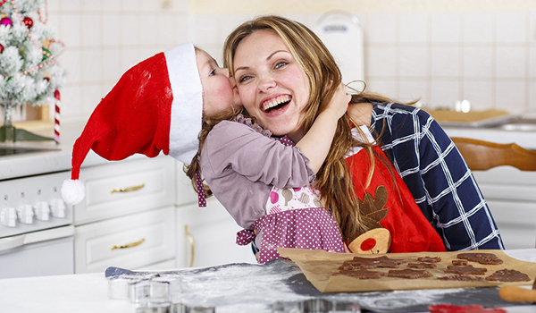 How to get your kids involved in christmas preparation - Child kissing her mother in the head happy while wearing a santa hat
