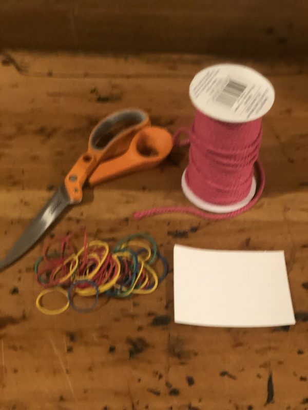 One Pink Tassles Placed in a wooden table with scissors and rubber bands and a piece of paper