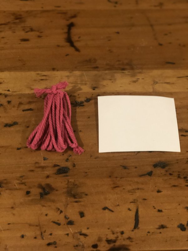One Pink Tassles Placed in a wooden table with a piece of paper beside it