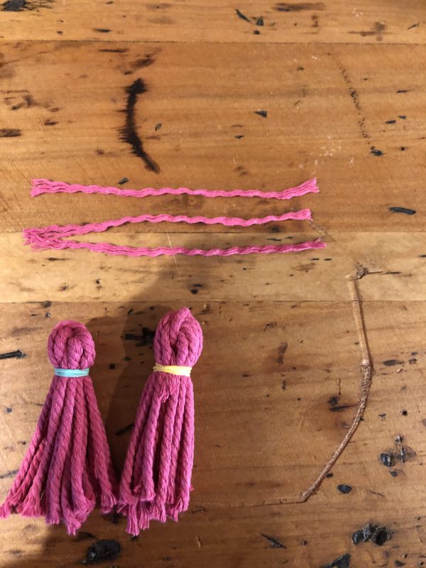 Two Pink Tassles Placed in a wooden table with an extra 3 strand of tassles