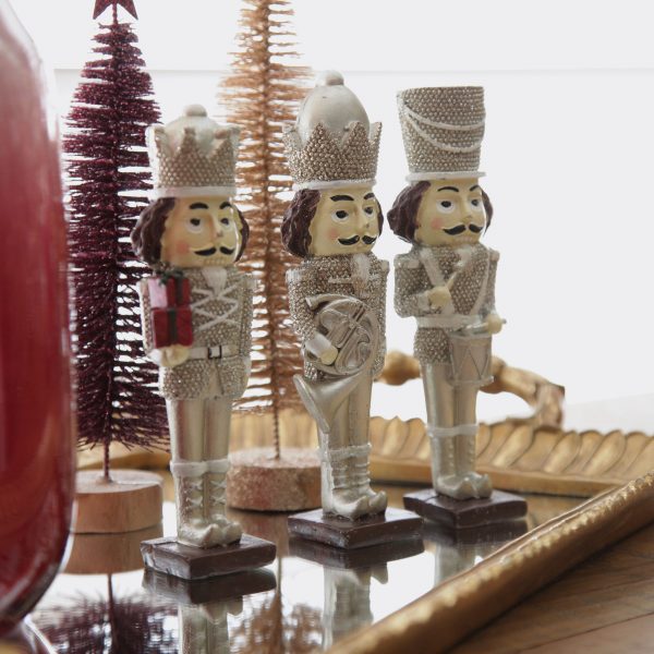 Three nutcrackers with Burgundy Bottle Brush tree and Gold Bottle Brush tree behind placed in a tray