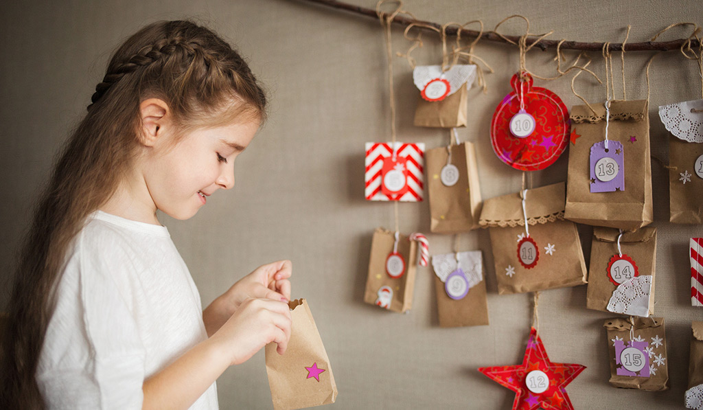 Little Girl Hanging something on a paper bag for the Advent Calendar While Smiling Featured Image