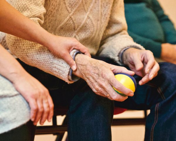 Person holding an old mans hands that is holding a small ball while sitting