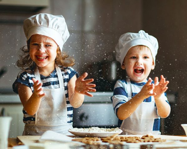 Girl and Boy Playing by baking christmas Cookies while wearing Chef hats and aprons