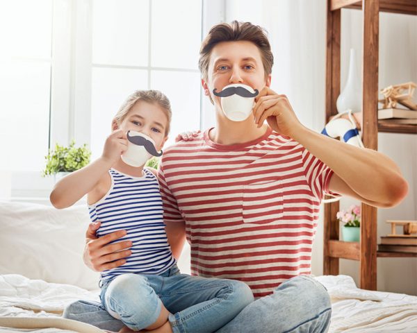 Father and daughter drinking a cup of beverage while wearing a fake paper mustache both are wearing a stripe shirt blue and red