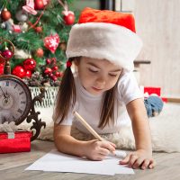 Little Girl Holding a Pencil and trying to draw while wearing a santa hat
