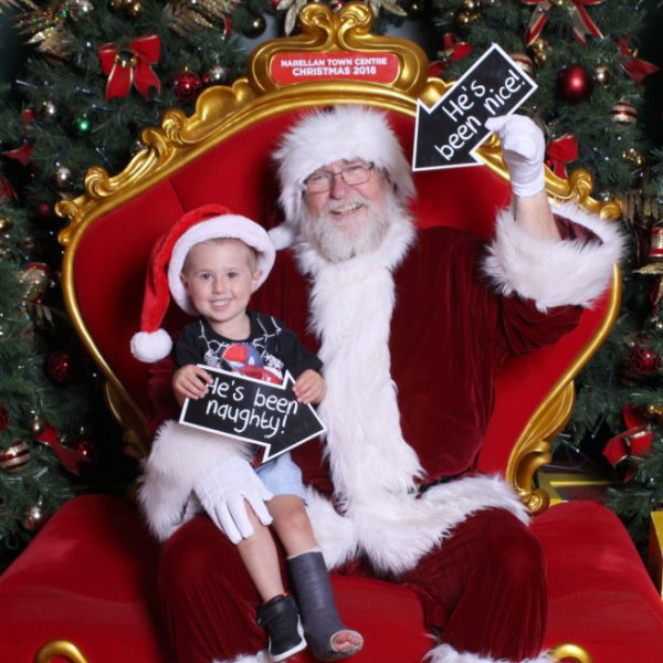 Visit Santa in Narellan Town Centre Santa Holding a little boy while he is holding a sign saying Hes been nice