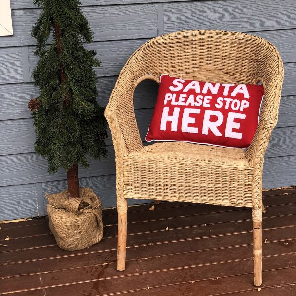 Santa Please stop here Cushion placed in a rattan chair beside a Small Tree outside the porch