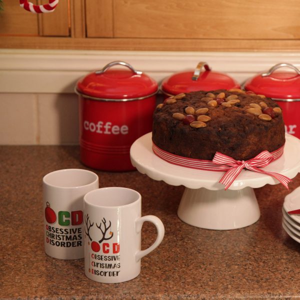 A Christmas Kitchen OCD Chritmas Mugs and a Cake with ribbon around placed in a kitchen table with three containers for coffee
