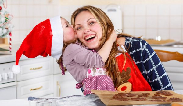 Daugter wearing her Santa hat kissing her mothers head both are wearing an apron and will bake some Christmas cookies