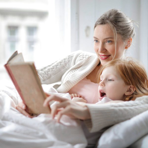 A mother reading a story book to her daughter while sitting on a sofa living room, mother wears her sweater