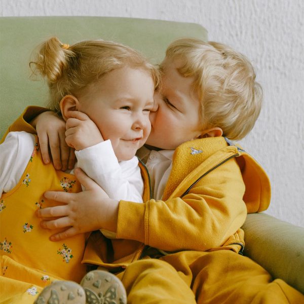 Little boy giving his sister a kiss on the cheek while hugging both are wearing bright yellow clothes