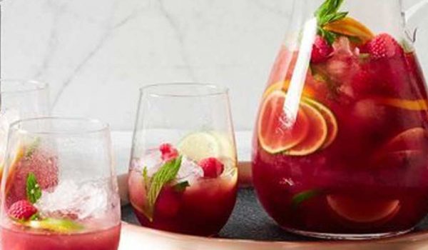 Red Sangria in pitcher & 2 glasses with orange, lime, lemon, & apple cut into thin wedges added raspberries and crushed ice
