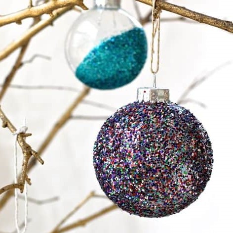 Purple Glittered Bauble hanging in a Branch also a blue half glittered bauble also hanging in the branch
