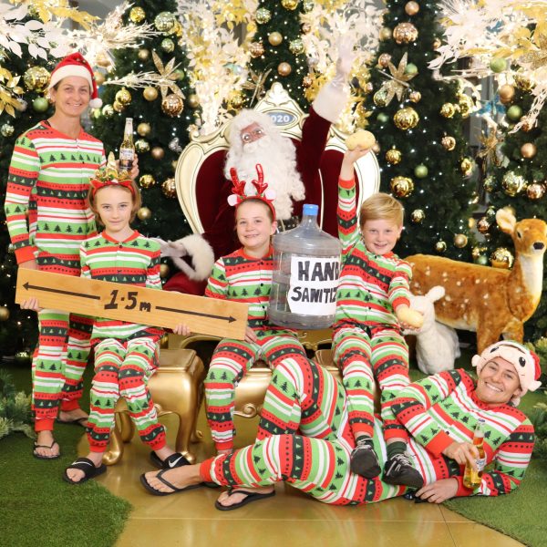 The whole family wearing christmas pajamas and holding a big water bottle and a measurement 1.5m with santa behind them
