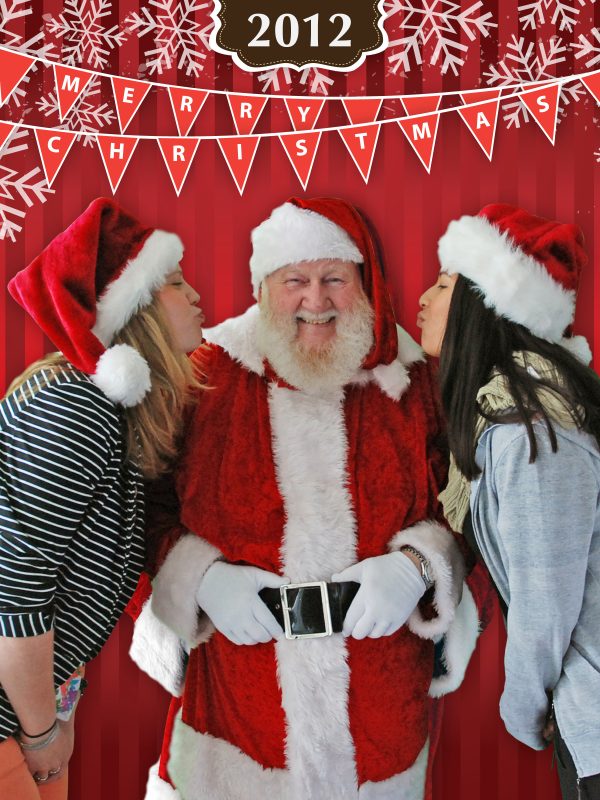 Santa with both girls beside him and trying to kiss him on the cheecks