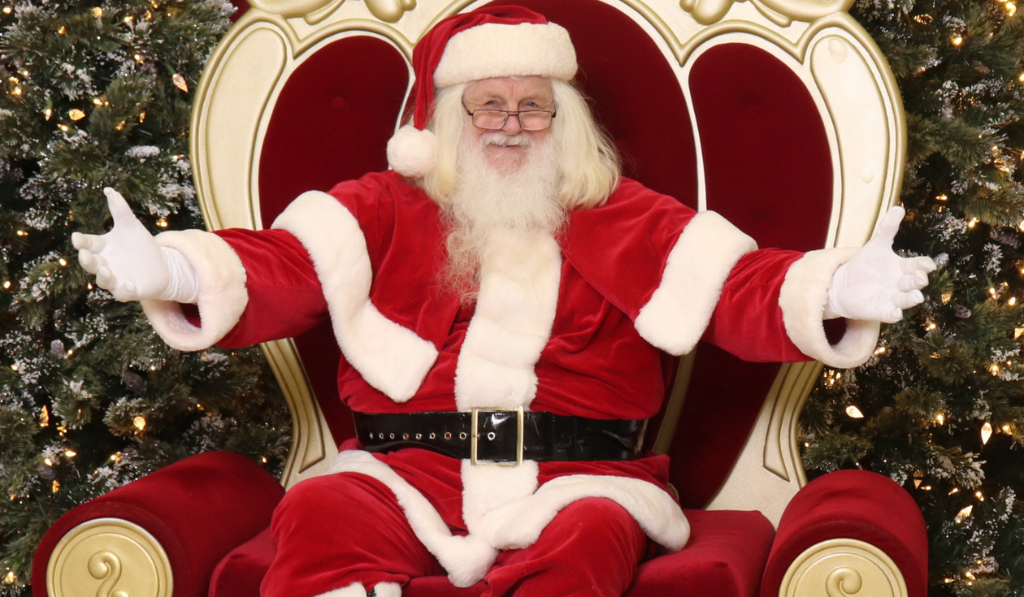 Santa sitting on hes big red chair and having his hands open to greet children or other visitors